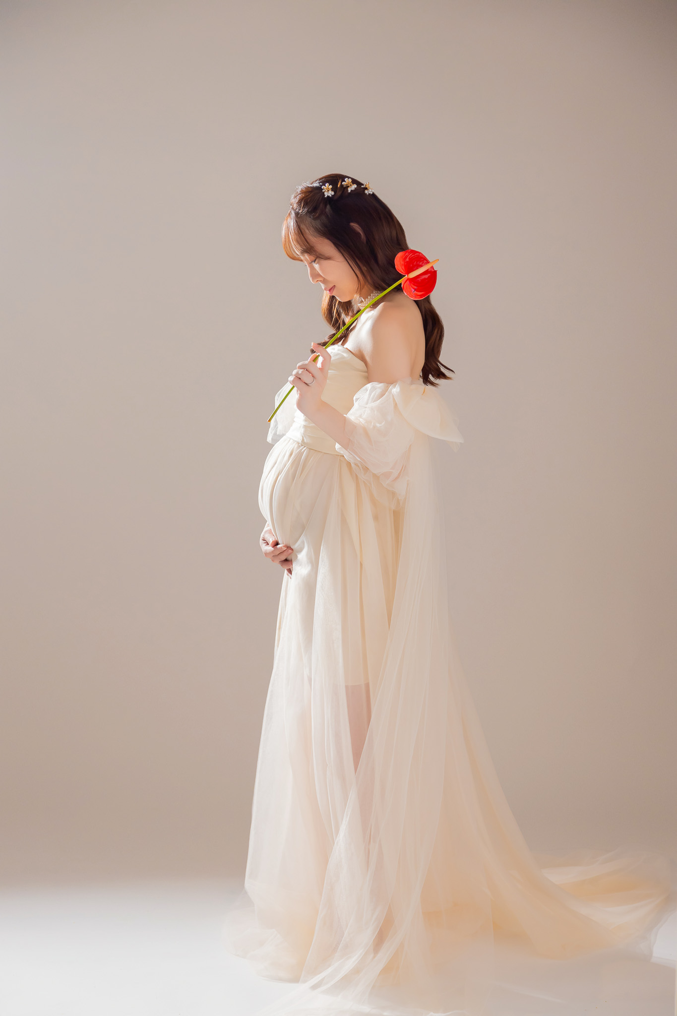 視線を落としてお腹を見つめる、クリーム色のドレスをまとった妊婦