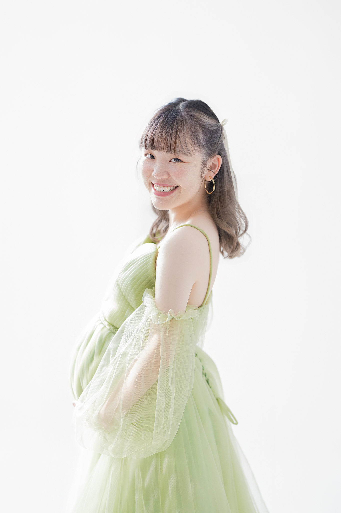 やわらかな光の中、グリーンのドレスをまとって自然な笑顔を見せる妊婦