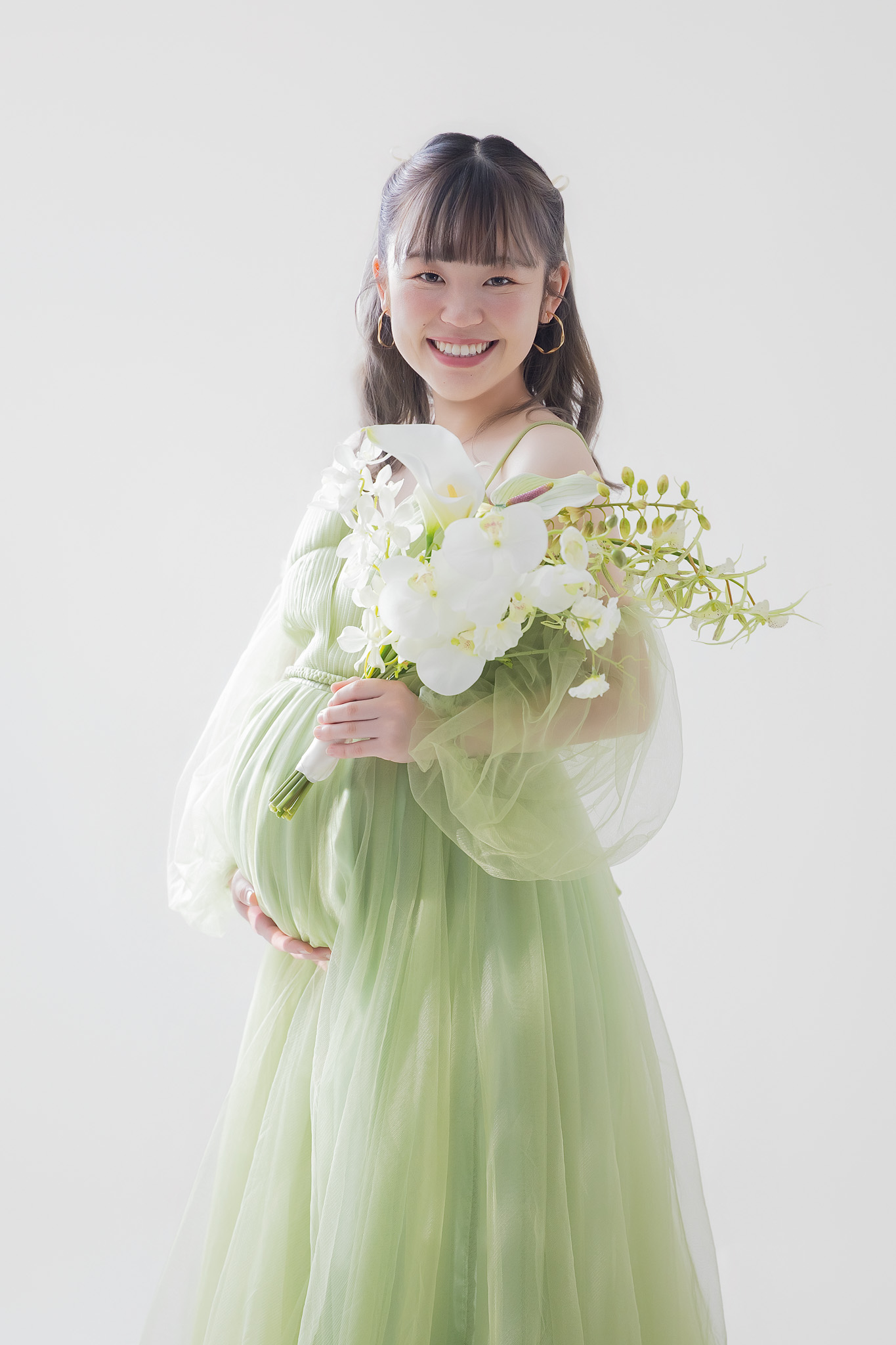 白いブーケを抱え、グリーンのドレスをまとって微笑む姿
