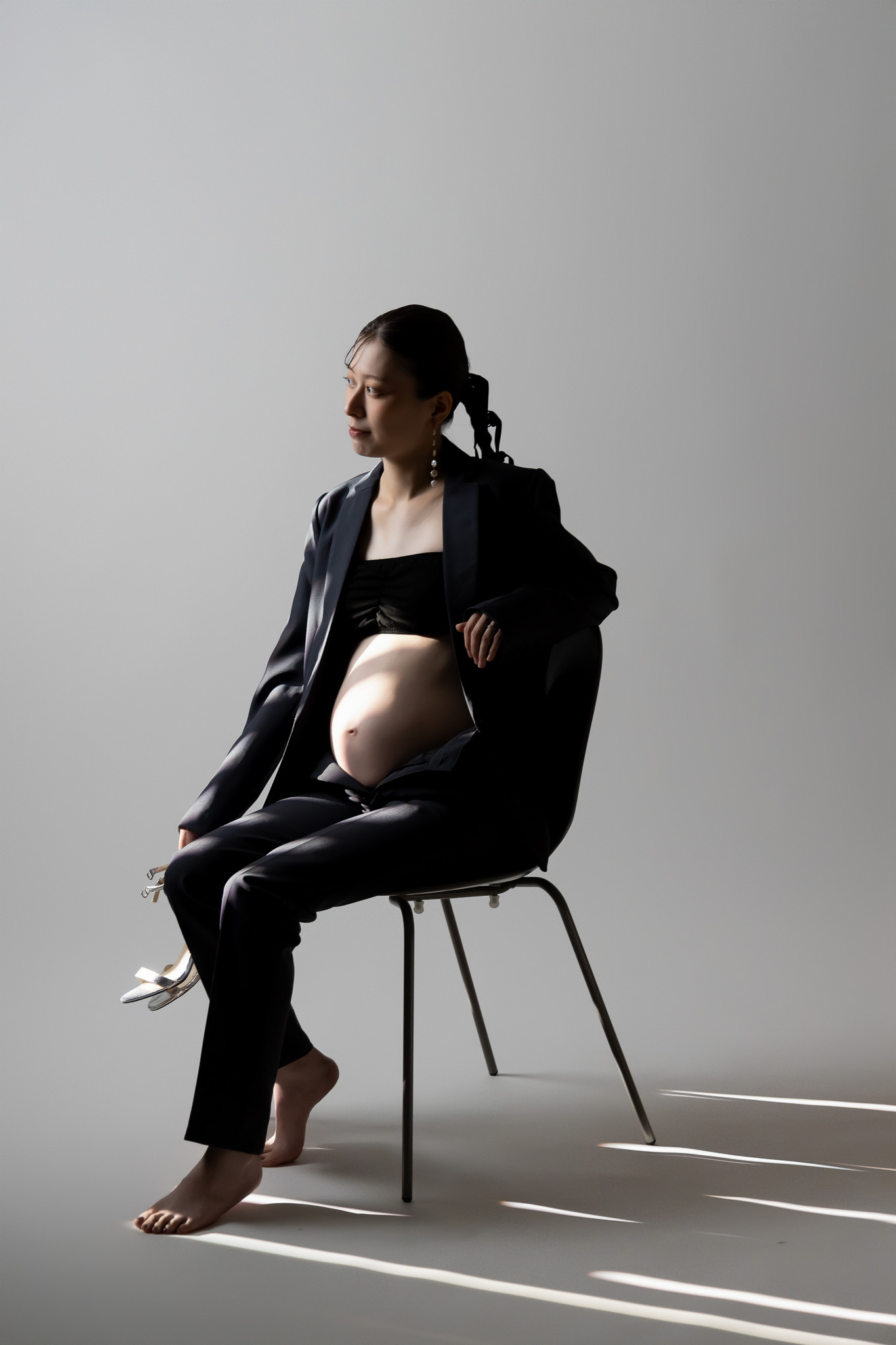窓からの光が差すスタジオで、椅子に腰かけてくつろぐ妊婦