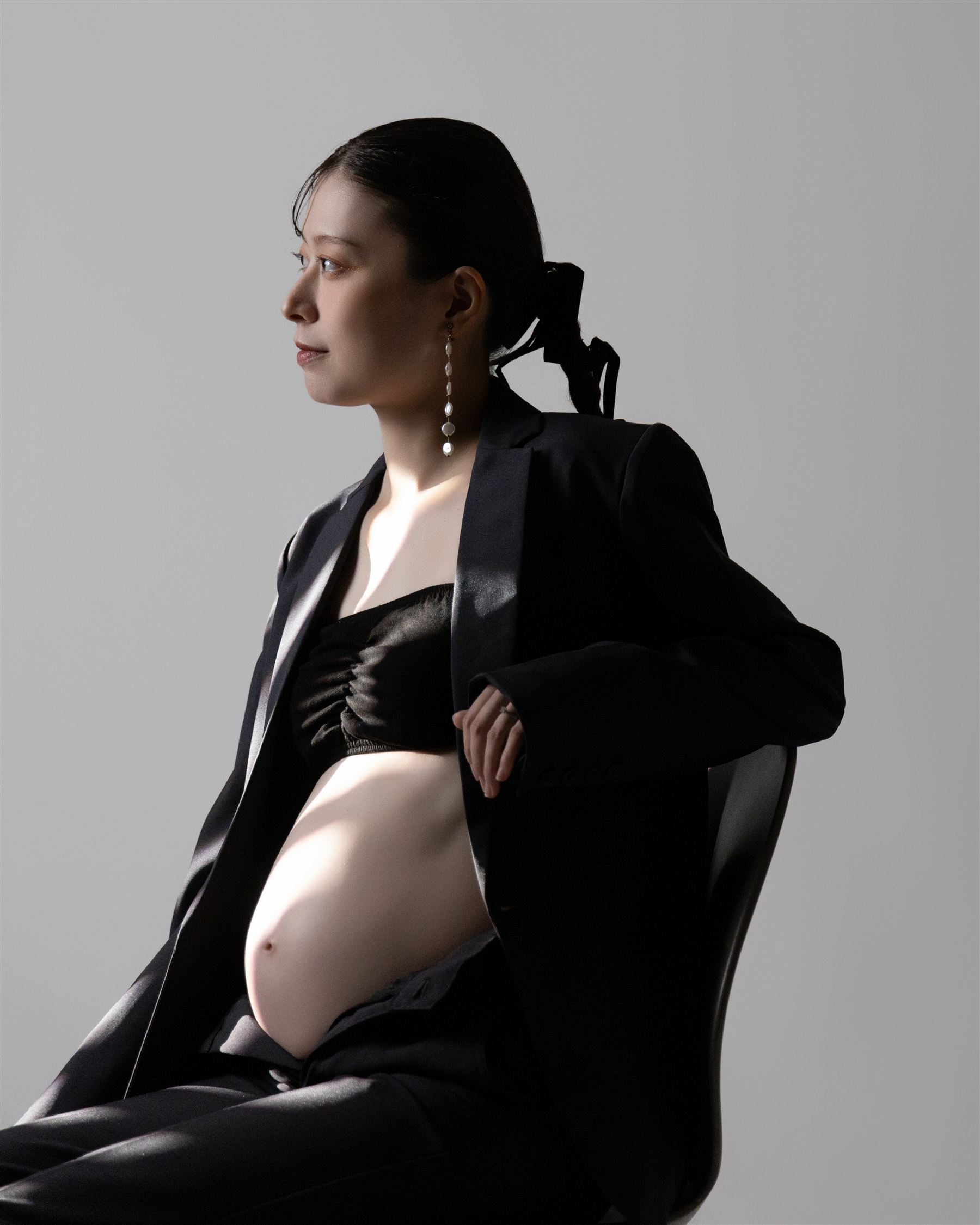 黒の装いで椅子に座り、静かに視線を向ける妊婦の姿