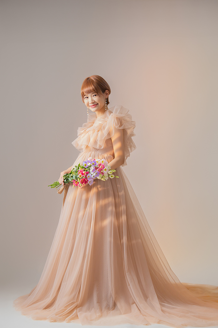 ピンクベージュのチュールドレス、花束を手に