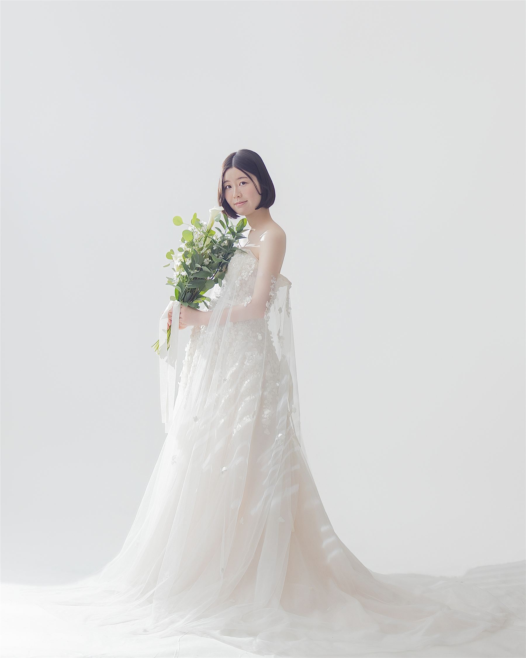 トレーンの長いドレスをまとい、花束を手にした妊婦の全身像