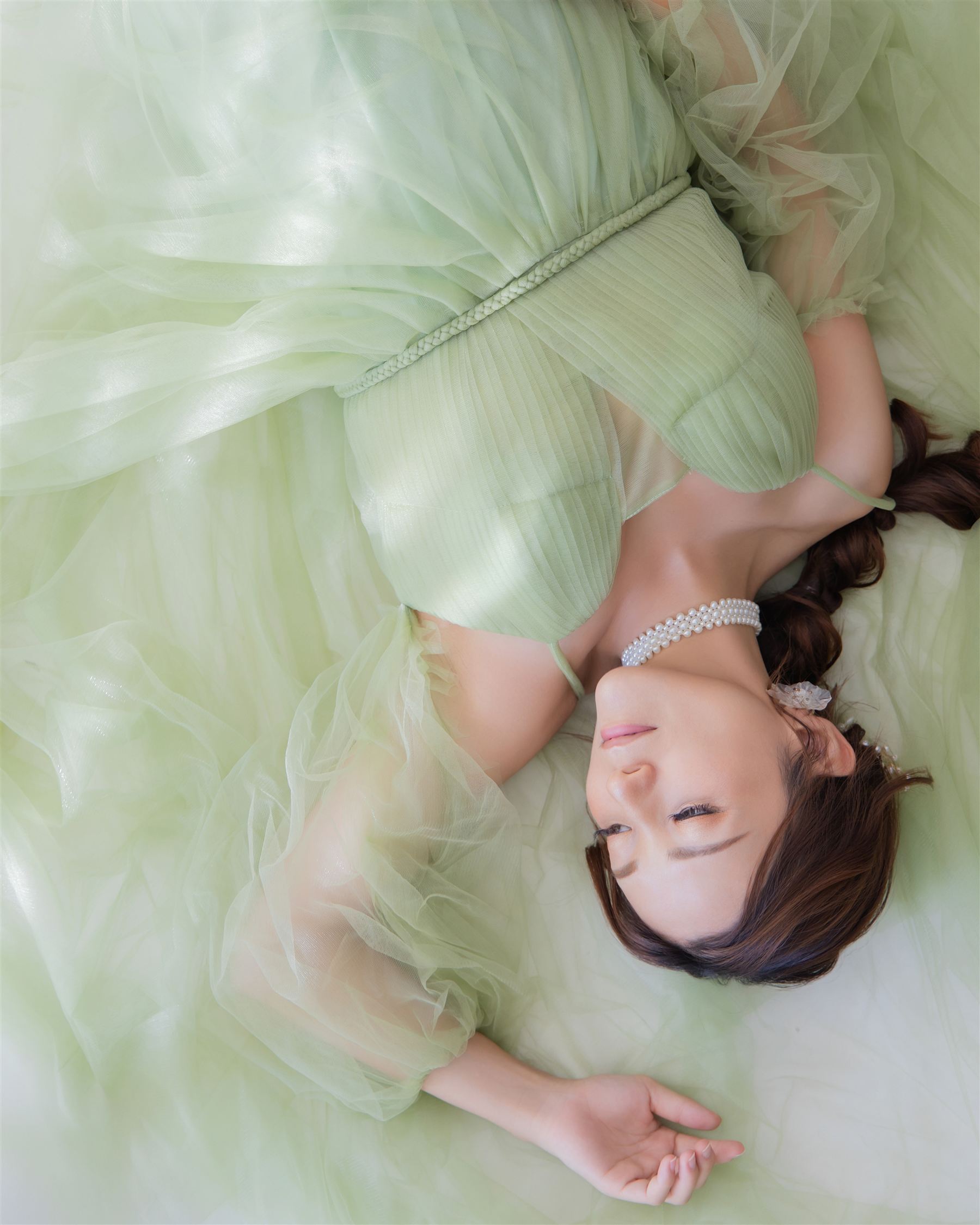 グリーンのドレスに横たわり、ヘアメイクを施した穏やかな表情