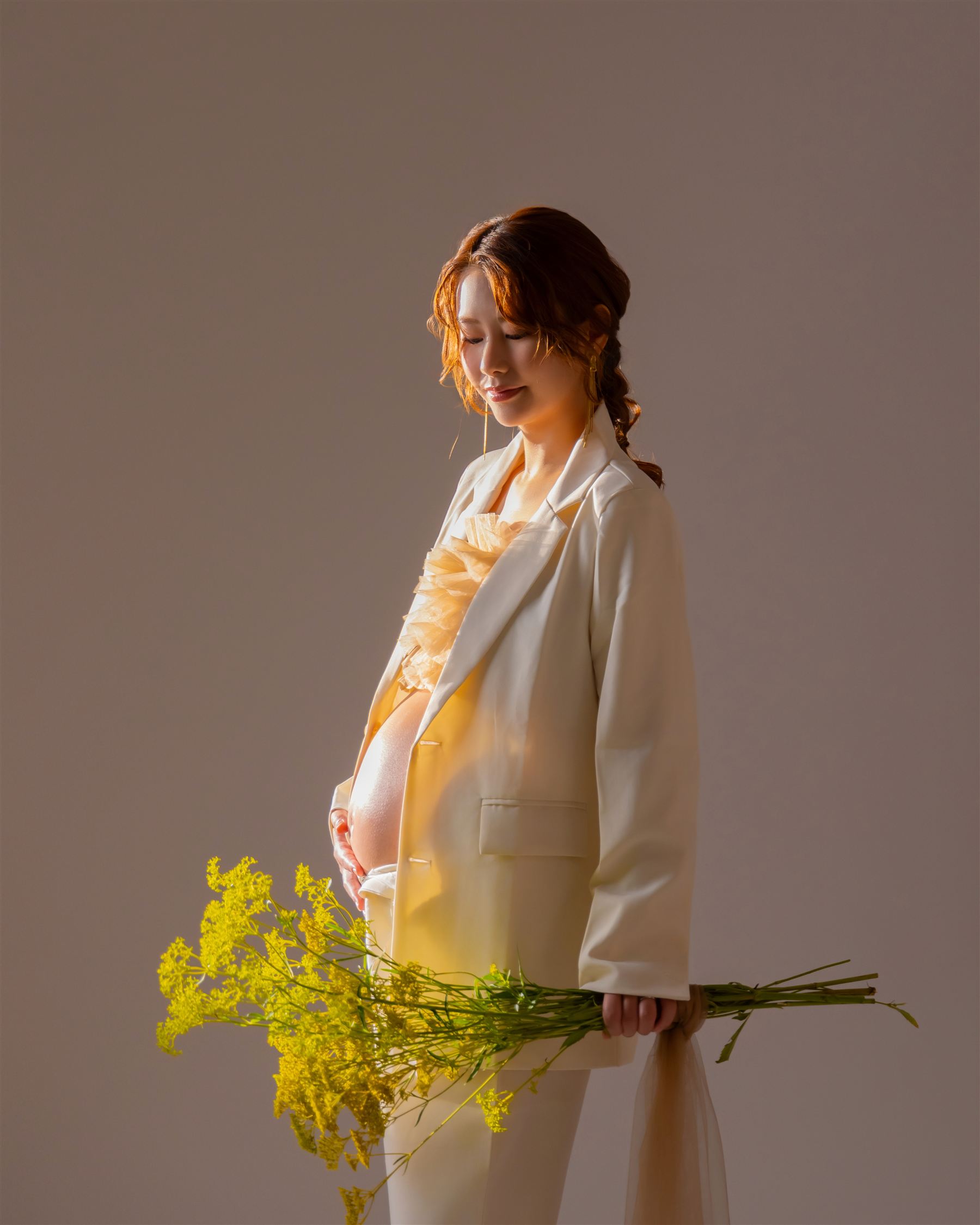 柔らかな逆光の中、お腹に手を添えて佇む妊婦の姿