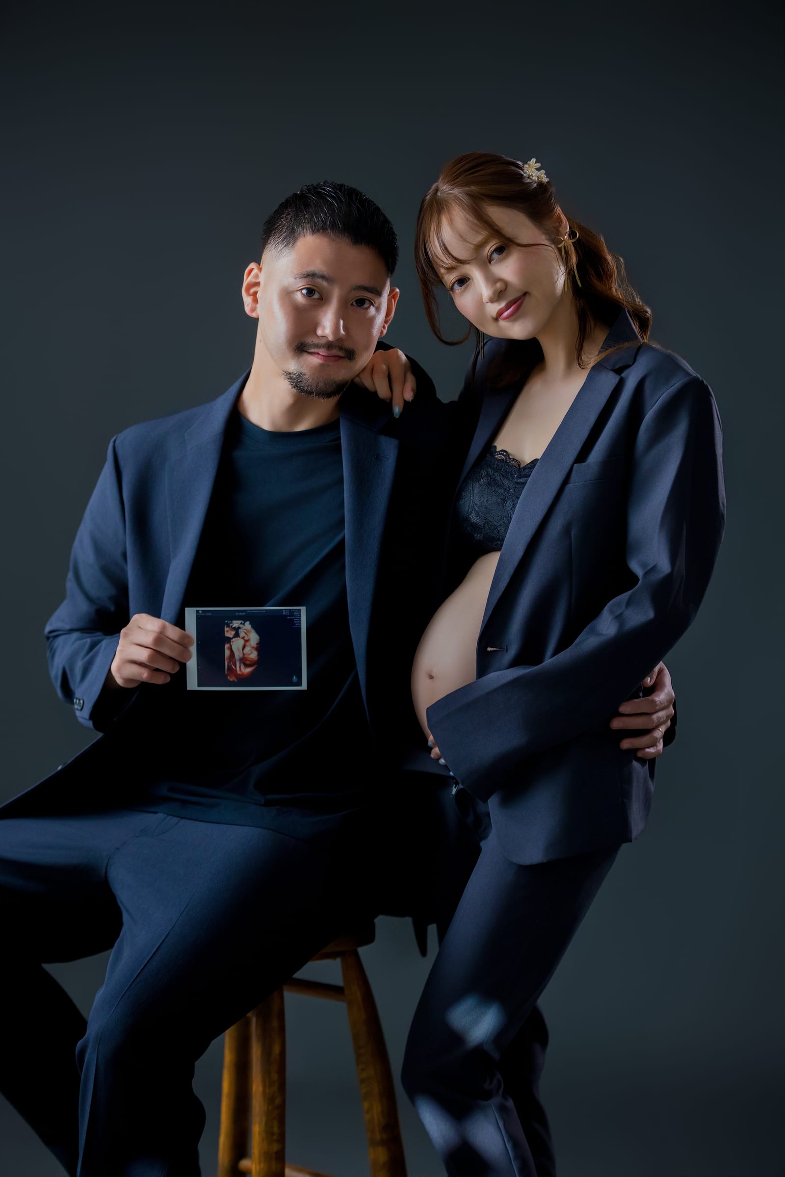 濃紺の衣装でエコー写真を手にする、スタジオでのご夫婦